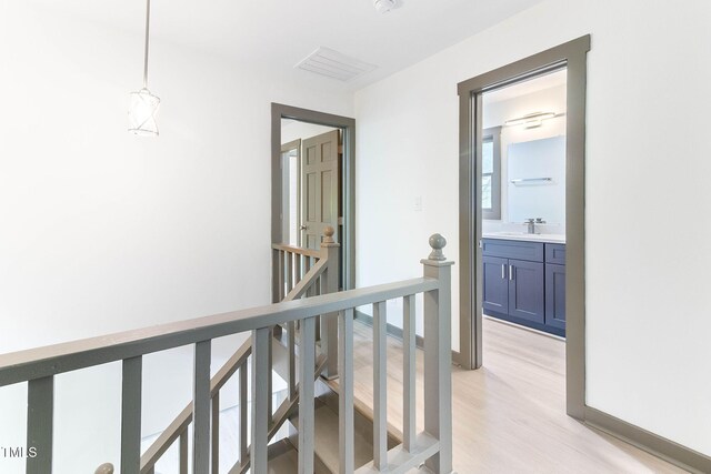 hall featuring an upstairs landing, light wood-style floors, baseboards, and a sink