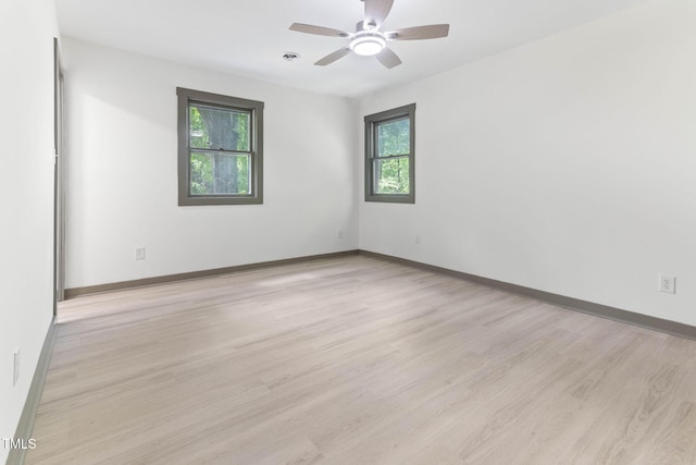 spare room featuring light wood-style flooring, a ceiling fan, and baseboards