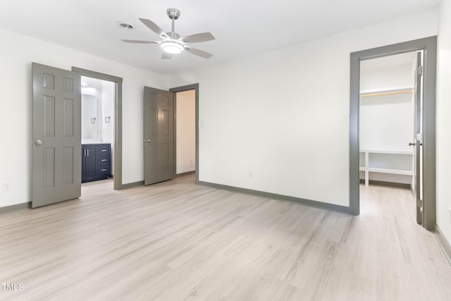 unfurnished bedroom featuring light wood finished floors, a walk in closet, baseboards, a closet, and ensuite bathroom