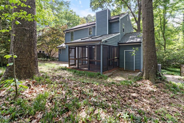 rear view of house with a sunroom, a chimney, and a shingled roof