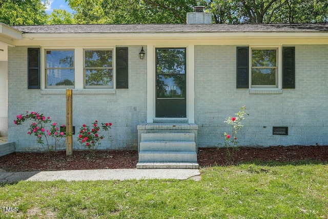 property entrance featuring a chimney, brick siding, a yard, and crawl space