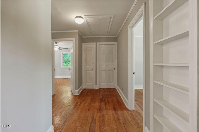 hall with ornamental molding, built in features, baseboards, attic access, and dark wood-style floors