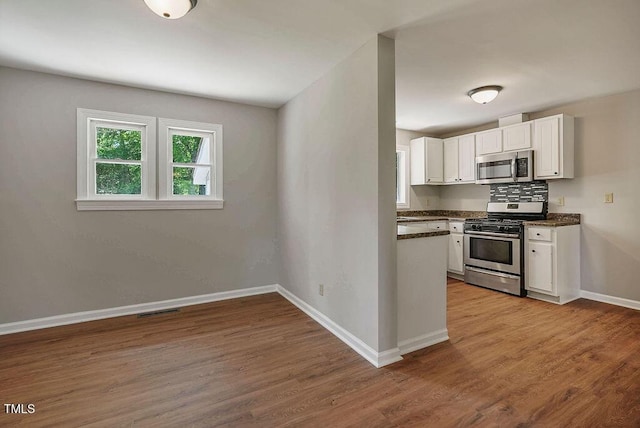 kitchen with white cabinets, dark countertops, stainless steel appliances, wood finished floors, and visible vents
