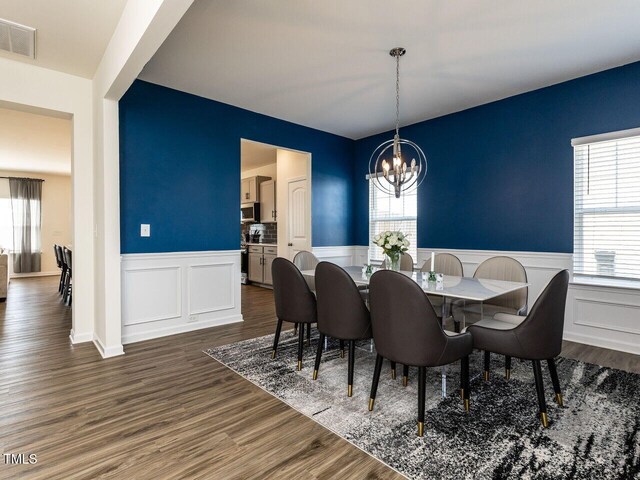 dining space featuring visible vents, wainscoting, dark wood finished floors, an inviting chandelier, and a decorative wall