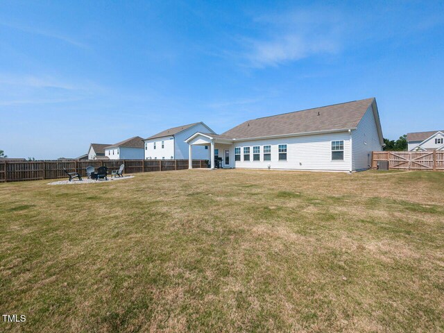 rear view of house featuring a lawn, a fire pit, and a fenced backyard