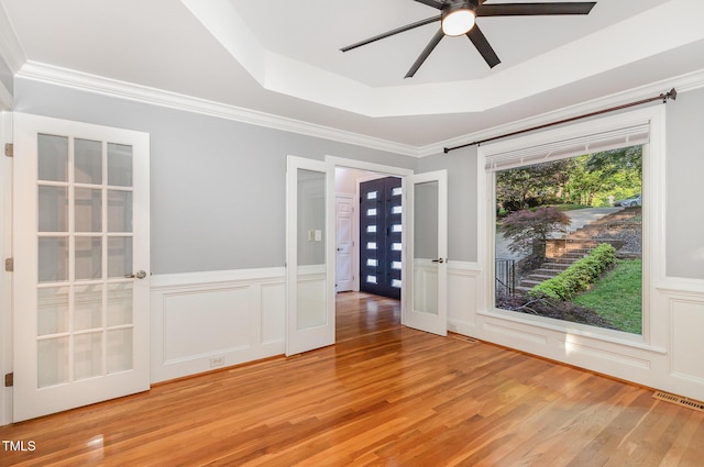 empty room with visible vents, a ceiling fan, light wood-style floors, and a tray ceiling