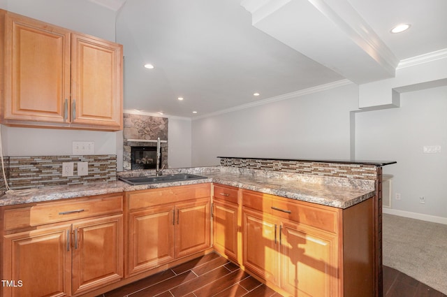 kitchen featuring a stone fireplace, crown molding, light stone countertops, a sink, and a peninsula