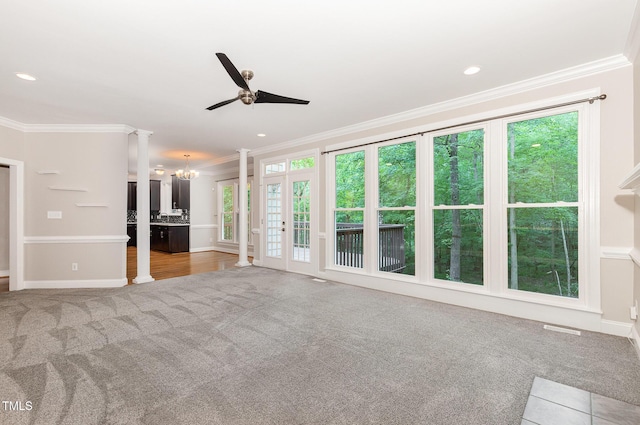 unfurnished living room featuring light colored carpet, ornamental molding, ceiling fan with notable chandelier, and a wealth of natural light