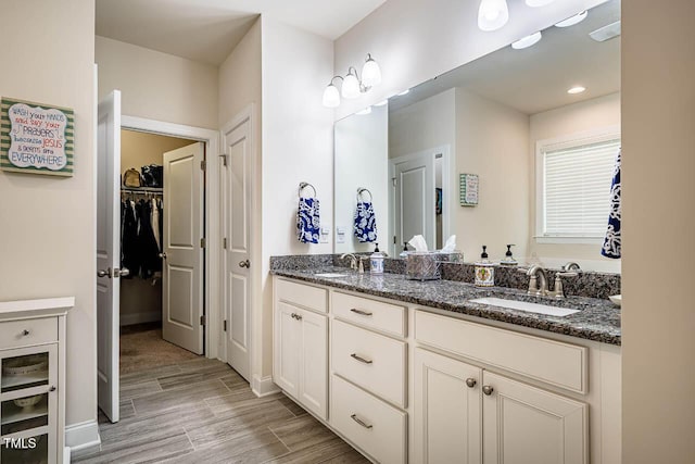 bathroom featuring double vanity, a spacious closet, a sink, and wood finished floors