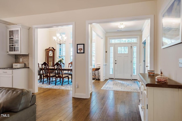 foyer entrance featuring dark wood-style floors, baseboards, a chandelier, and ornamental molding