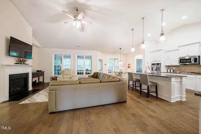 living area with ceiling fan, high vaulted ceiling, recessed lighting, a fireplace with flush hearth, and dark wood finished floors