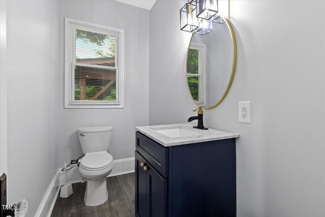 half bath featuring baseboards, vanity, toilet, and wood finished floors