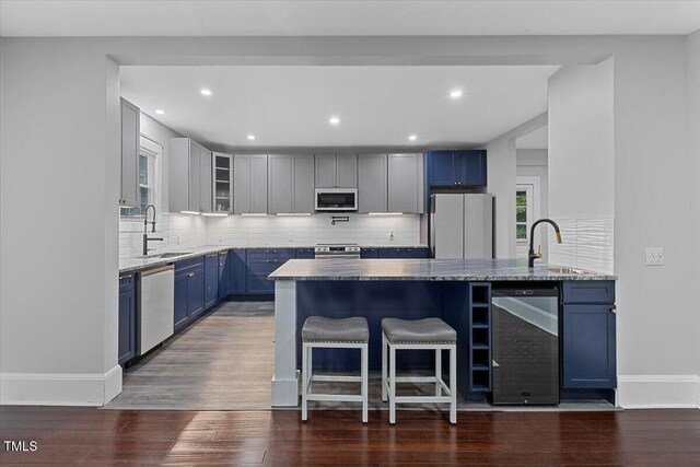 kitchen featuring wine cooler, a peninsula, stainless steel appliances, a sink, and blue cabinetry