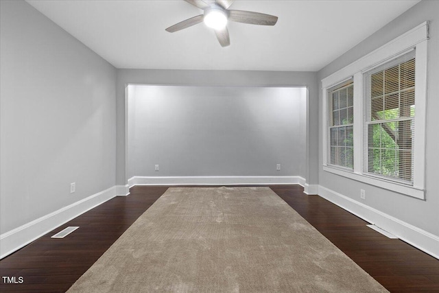 spare room featuring baseboards, a ceiling fan, dark wood-style flooring, and visible vents