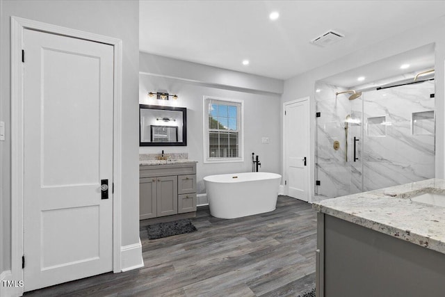 bathroom with a freestanding tub, wood finished floors, vanity, a marble finish shower, and recessed lighting