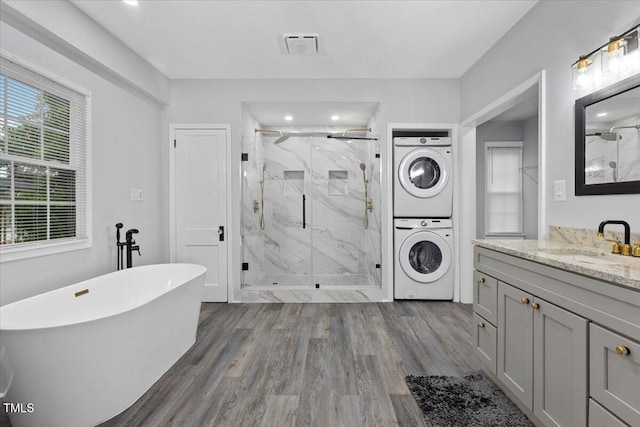 bathroom featuring stacked washer and clothes dryer, a marble finish shower, wood finished floors, and a freestanding tub