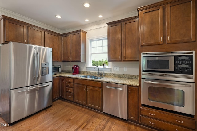 kitchen with light stone countertops, wood finished floors, a sink, ornamental molding, and stainless steel appliances