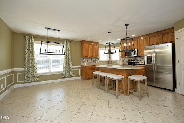 kitchen featuring appliances with stainless steel finishes, brown cabinetry, a center island, light tile patterned floors, and backsplash