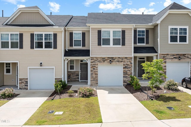 townhome / multi-family property featuring stone siding, concrete driveway, a front lawn, and an attached garage