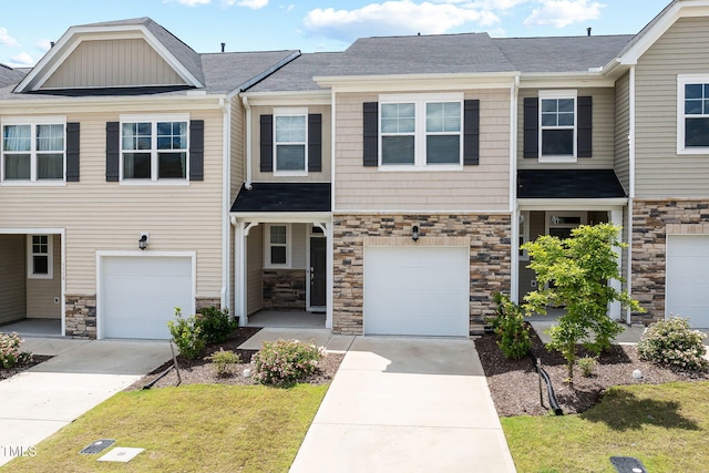 townhome / multi-family property with driveway, stone siding, a garage, and a front lawn