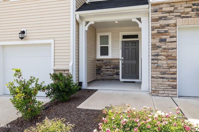 view of exterior entry featuring stone siding, a garage, and a shingled roof
