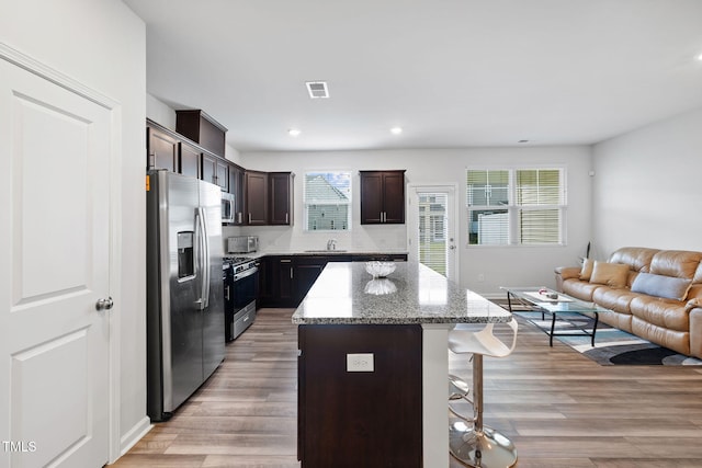kitchen with appliances with stainless steel finishes, a breakfast bar area, open floor plan, a kitchen island, and light wood-type flooring