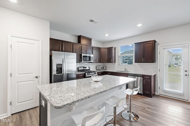 kitchen featuring stainless steel appliances, a breakfast bar area, dark brown cabinetry, a kitchen island, and light wood-style flooring