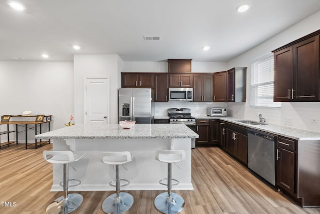 kitchen with appliances with stainless steel finishes, a center island, a kitchen breakfast bar, tasteful backsplash, and dark brown cabinetry