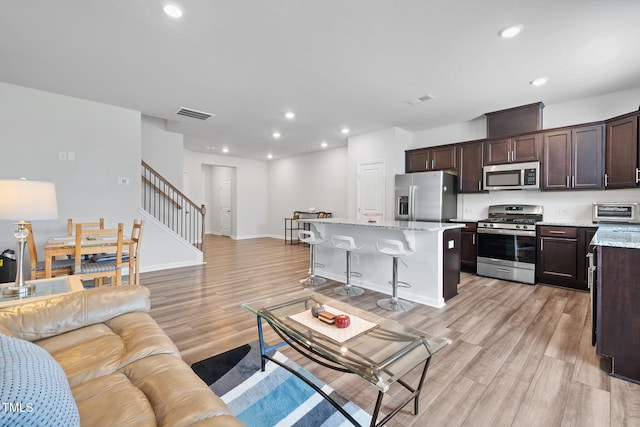 living room featuring stairs, light wood-type flooring, recessed lighting, and baseboards