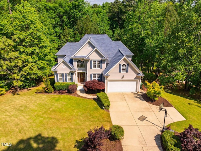 traditional-style house featuring a forest view, driveway, a shingled roof, and a front yard