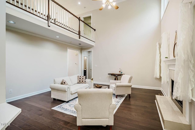 living area featuring a towering ceiling, hardwood / wood-style floors, baseboards, a ceiling fan, and a premium fireplace