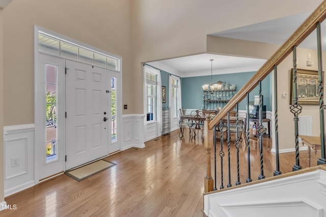 foyer entrance with crown molding, a wainscoted wall, a notable chandelier, a decorative wall, and hardwood / wood-style floors