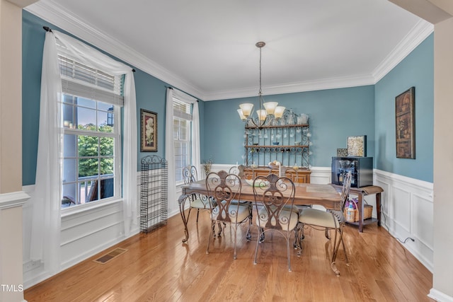 dining area with visible vents, wood finished floors, a wainscoted wall, an inviting chandelier, and ornamental molding