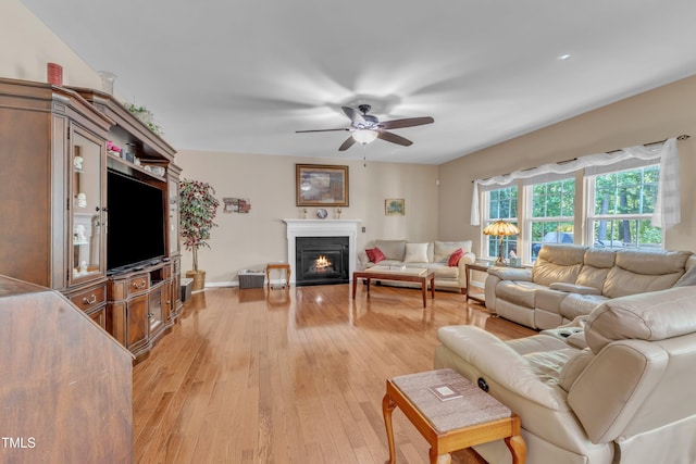 living room with light wood-style floors, a ceiling fan, baseboards, and a glass covered fireplace