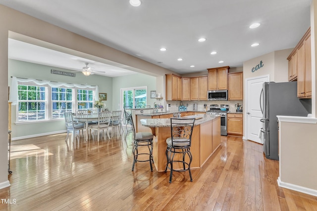 kitchen featuring ceiling fan, appliances with stainless steel finishes, light stone counters, light wood-style floors, and recessed lighting
