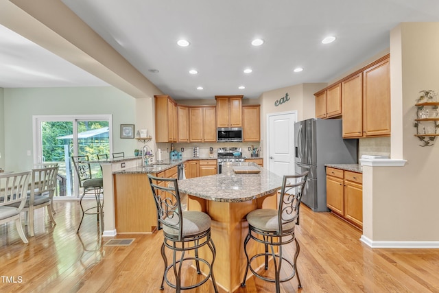kitchen featuring stainless steel appliances, a peninsula, a kitchen breakfast bar, and light wood-style floors
