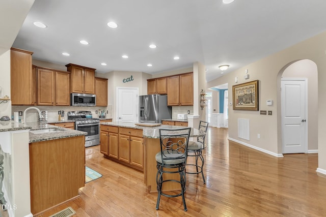 kitchen featuring a breakfast bar area, appliances with stainless steel finishes, arched walkways, light stone countertops, and a sink