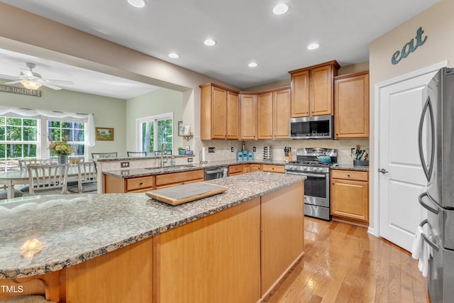 kitchen with appliances with stainless steel finishes, a sink, light stone counters, a peninsula, and light wood-style floors