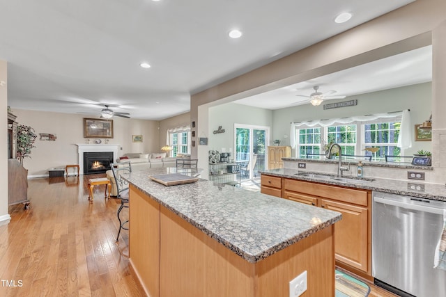 kitchen with a sink, a ceiling fan, open floor plan, stainless steel dishwasher, and a lit fireplace