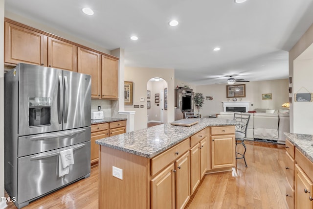kitchen with ceiling fan, stainless steel fridge, light wood finished floors, arched walkways, and a center island