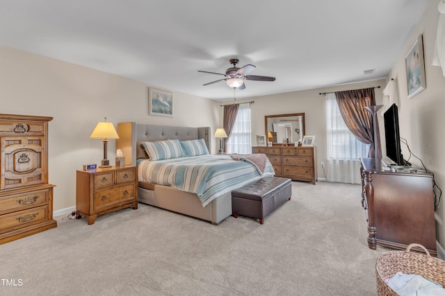 bedroom featuring baseboards, a ceiling fan, light carpet, and multiple windows