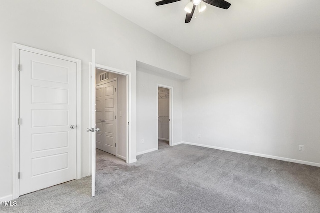 unfurnished bedroom with a walk in closet, visible vents, vaulted ceiling, baseboards, and carpet flooring