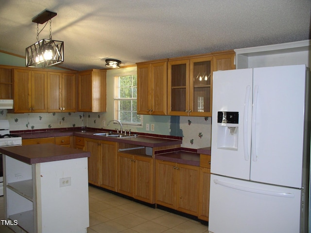 kitchen with brown cabinets, exhaust hood, dark countertops, a sink, and white appliances