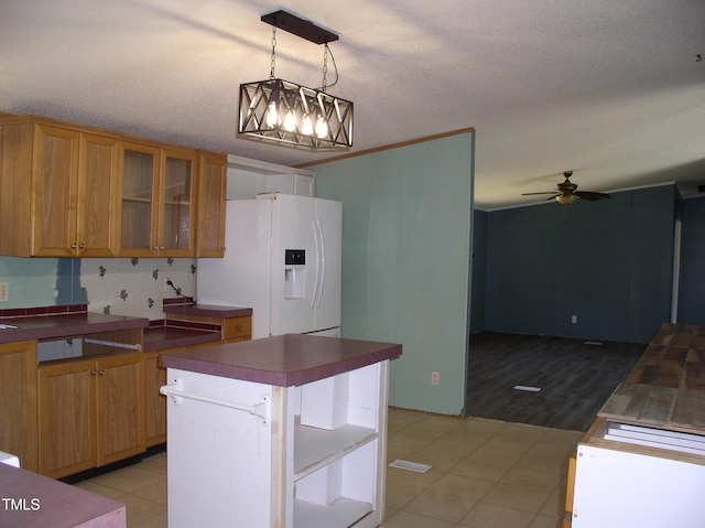 kitchen with ceiling fan, brown cabinetry, dark countertops, white refrigerator with ice dispenser, and glass insert cabinets