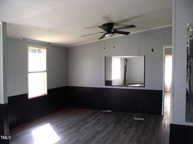 spare room with a textured ceiling, ceiling fan, wood finished floors, and a wainscoted wall