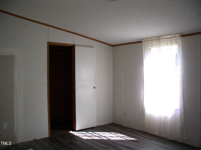 empty room with ornamental molding, vaulted ceiling, a textured ceiling, and wood finished floors