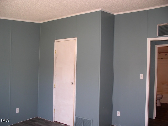 empty room featuring dark wood-style floors, a textured ceiling, visible vents, and ornamental molding