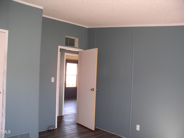 unfurnished room with crown molding, dark wood-style flooring, a textured ceiling, and visible vents