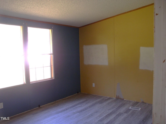 unfurnished room with crown molding, a textured ceiling, wood finished floors, and visible vents