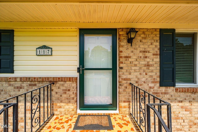 doorway to property with covered porch and brick siding
